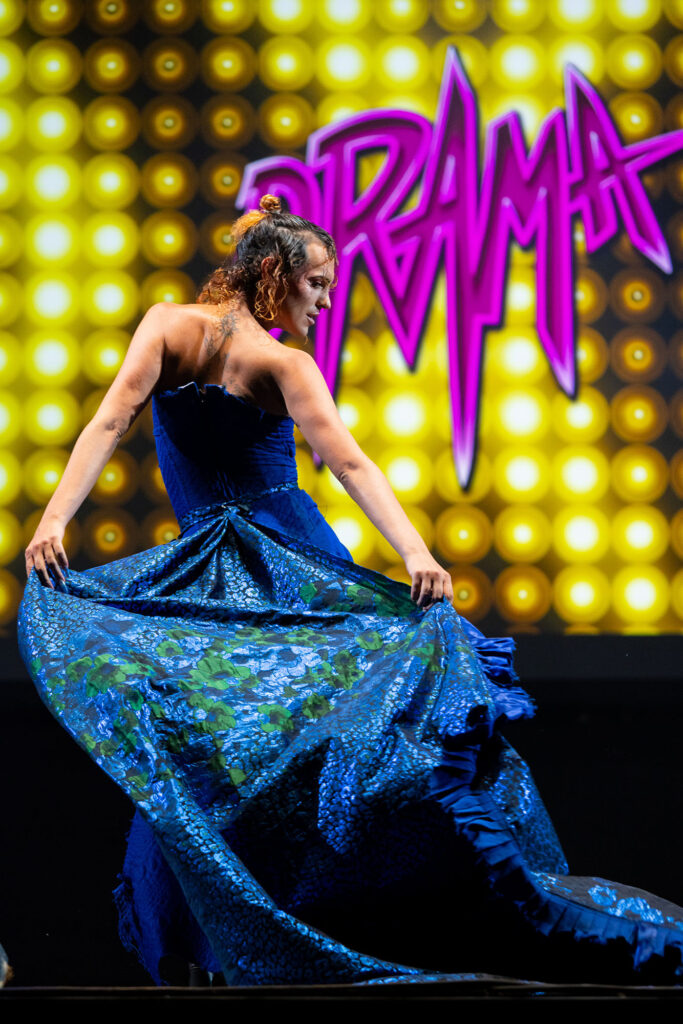 Performer in abito blu davanti al logo DRAMA